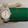 Silver Rolex watch on a white cloth with a green warranty card in the background
